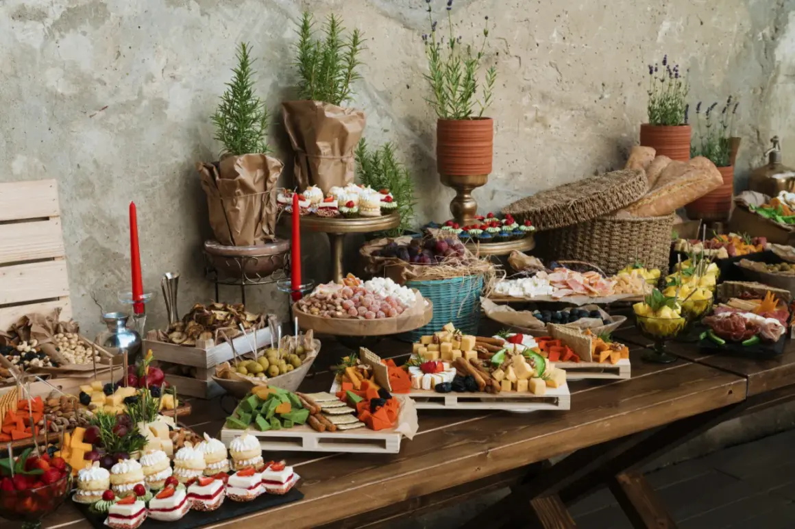 Bogaty stół z przekąskami: sery, owoce, ciastka, pieczywo. Zastanawiasz się, ile kosztuje catering na 20 osób? To bogactwo smaków!